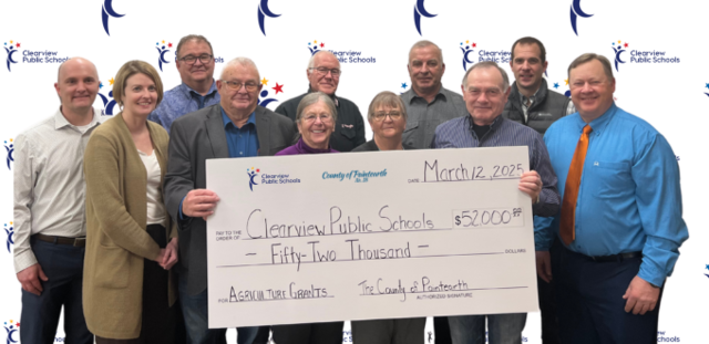 A group of representatives from Clearview Public Schools and the County of Paintearth stand together holding an oversized check for $52,000, dated March 12, 2025. The check is designated for Agriculture Trailer Upgrades. The background features a Clearvie