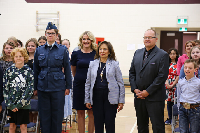 Her Honour Salma Lakhani, Lieutenant Governor of Alberta, stands in a school gymnasium alongside students, teacher Celene Rajewski, and Principal Jeff Lee at Erskine School. Flight Corporal Hudson Hetchler is also pictured in uniform. They are surrounded