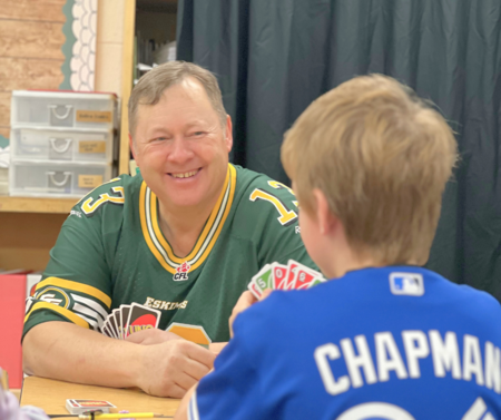 Clearview Trustee smiling and engaged in a friendly card game with a student during a school visit, fostering community and connection.